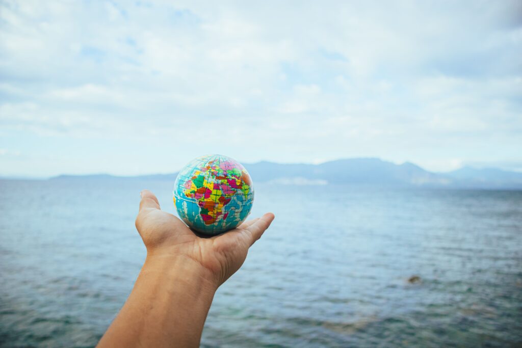 Ma tunnen kaasa, aga ma ei kanna enam kogu maailma oma õlgadel. A hand holds a small globe with a scenic ocean backdrop, symbolizing global exploration.