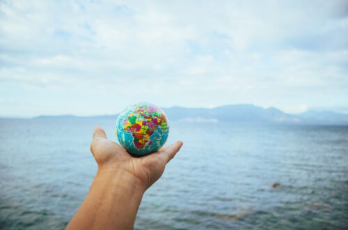 Ma tunnen kaasa, aga ma ei kanna enam kogu maailma oma õlgadel. A hand holds a small globe with a scenic ocean backdrop, symbolizing global exploration.