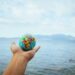 Ma tunnen kaasa, aga ma ei kanna enam kogu maailma oma õlgadel. A hand holds a small globe with a scenic ocean backdrop, symbolizing global exploration.