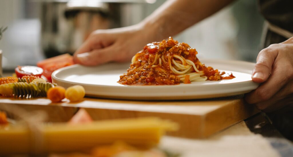 Rohkem kui lihtsalt kohvik – kuidas maailma maitsed õpetasid erivajadustega inimestele iseseisvust ja eluks vajalikke oskusi Crop anonymous chef taking portion of delicious pasta with sauce while cooking lunch in kitchen