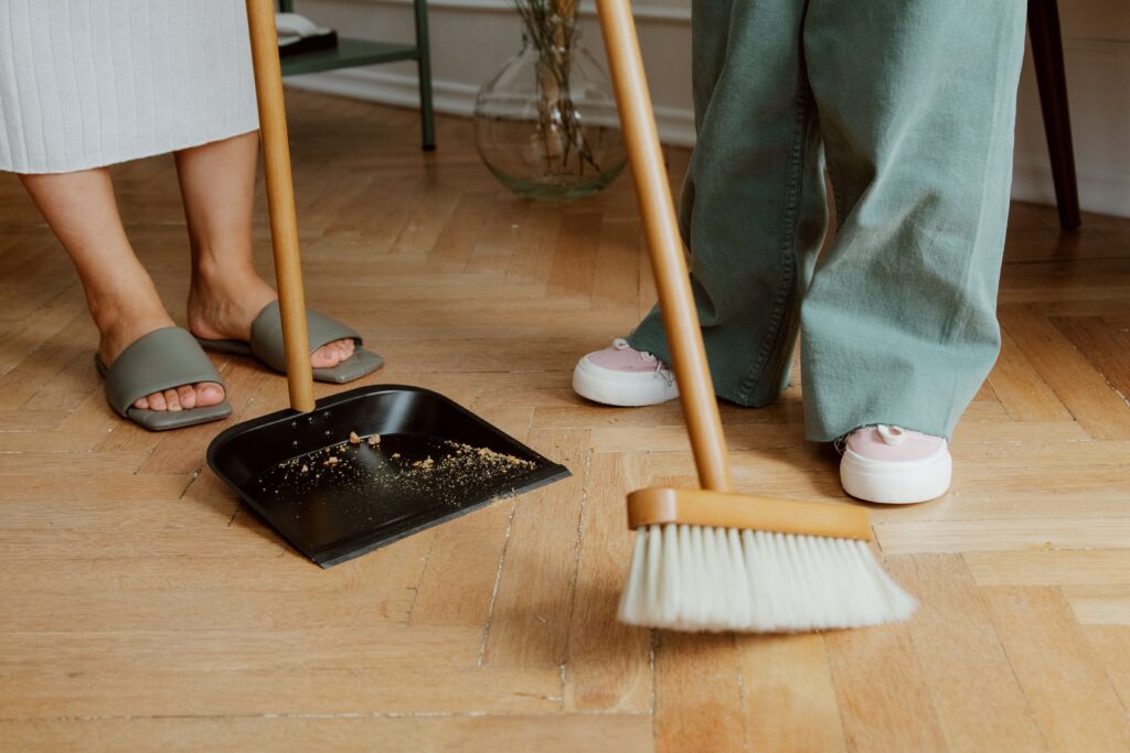 Kuidas hinnatakse kogukonnateenuse kvaliteeti Close-up of people cleaning wooden floor with broom and dustpan indoors.