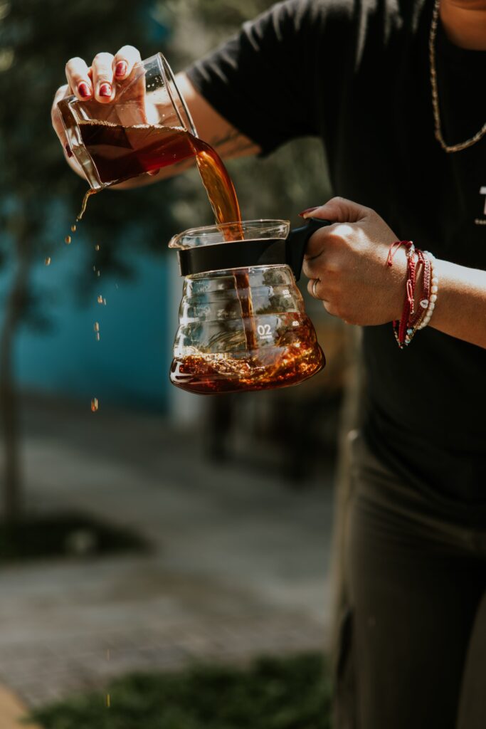 Mõnikord just nii paranemine välja näebki. A person pouring fresh coffee into a glass jug in an outdoor setting with greenery.