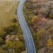 Aerial shot of a winding rural road surrounded by autumn trees, showcasing nature's vibrant colors.