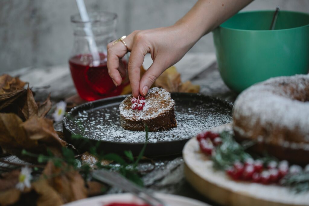 Crop unrecognizable female decorating sweet fresh pie slice with ripe red currant on table