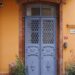 Victorian blue metal door set in red brick facade, framed by vibrant orange wall.