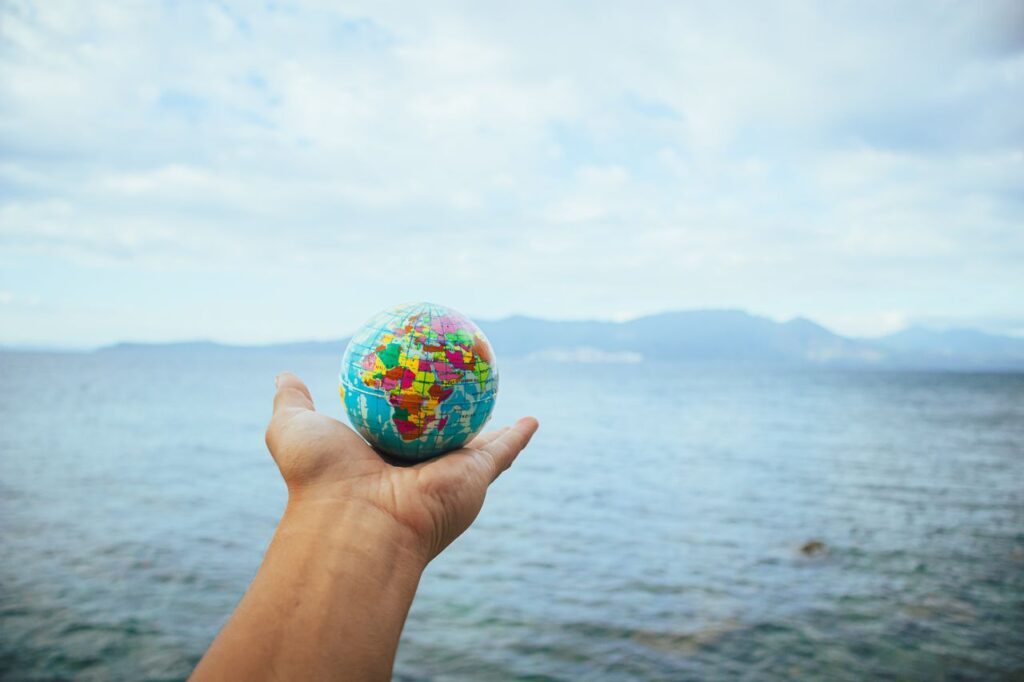 A hand holds a small globe with a scenic ocean backdrop, symbolizing global exploration.