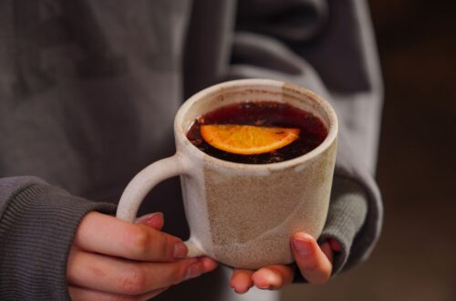 Warm close-up of a person holding a tea mug with a slice of lemon. Perfect for cozy autumn vibes.