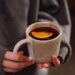 Warm close-up of a person holding a tea mug with a slice of lemon. Perfect for cozy autumn vibes.