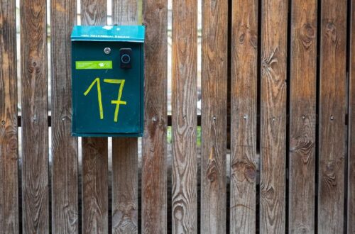 A green mailbox numbered 17 on a rustic wooden fence, creating a vintage outdoor feel.