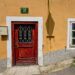 A rustic red door with iron bars set in a yellow stucco wall, reflecting European architectural charm.