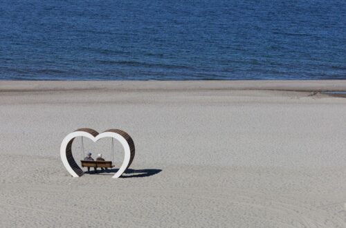 A serene scene of an elderly couple sitting on a bench by the sea, embraced by a heart-shaped structure.