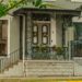 Victorian porch with intricate wrought iron design, adorned with wreaths and plants, evoking classic charm.