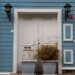 Charming blue house exterior with white door, potted plants, and wall lamps.